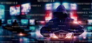 An image of a hooded man sitting in front of a computer committing click fraud.